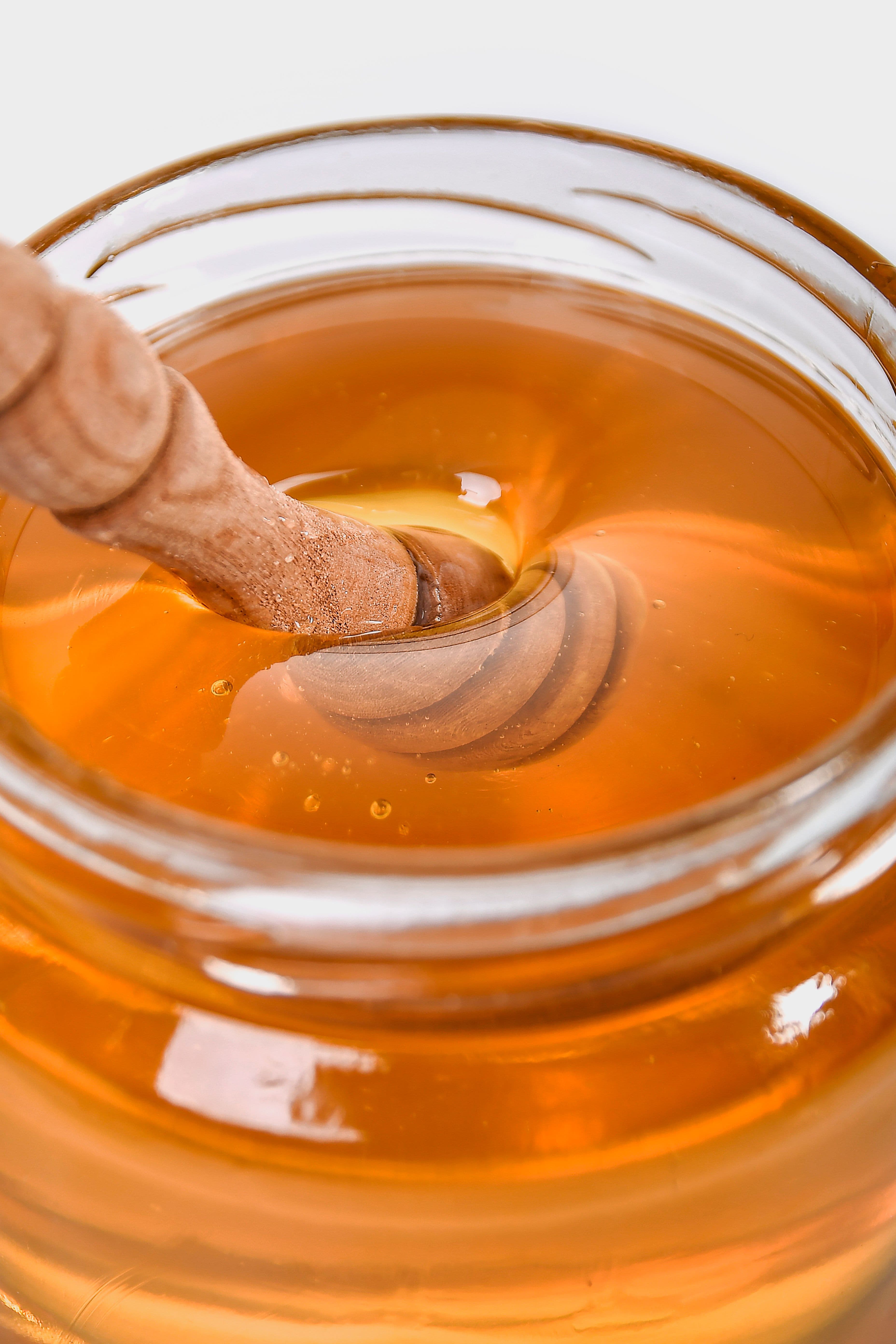 A wooden honey dipper submerged in a glass jar of golden honey