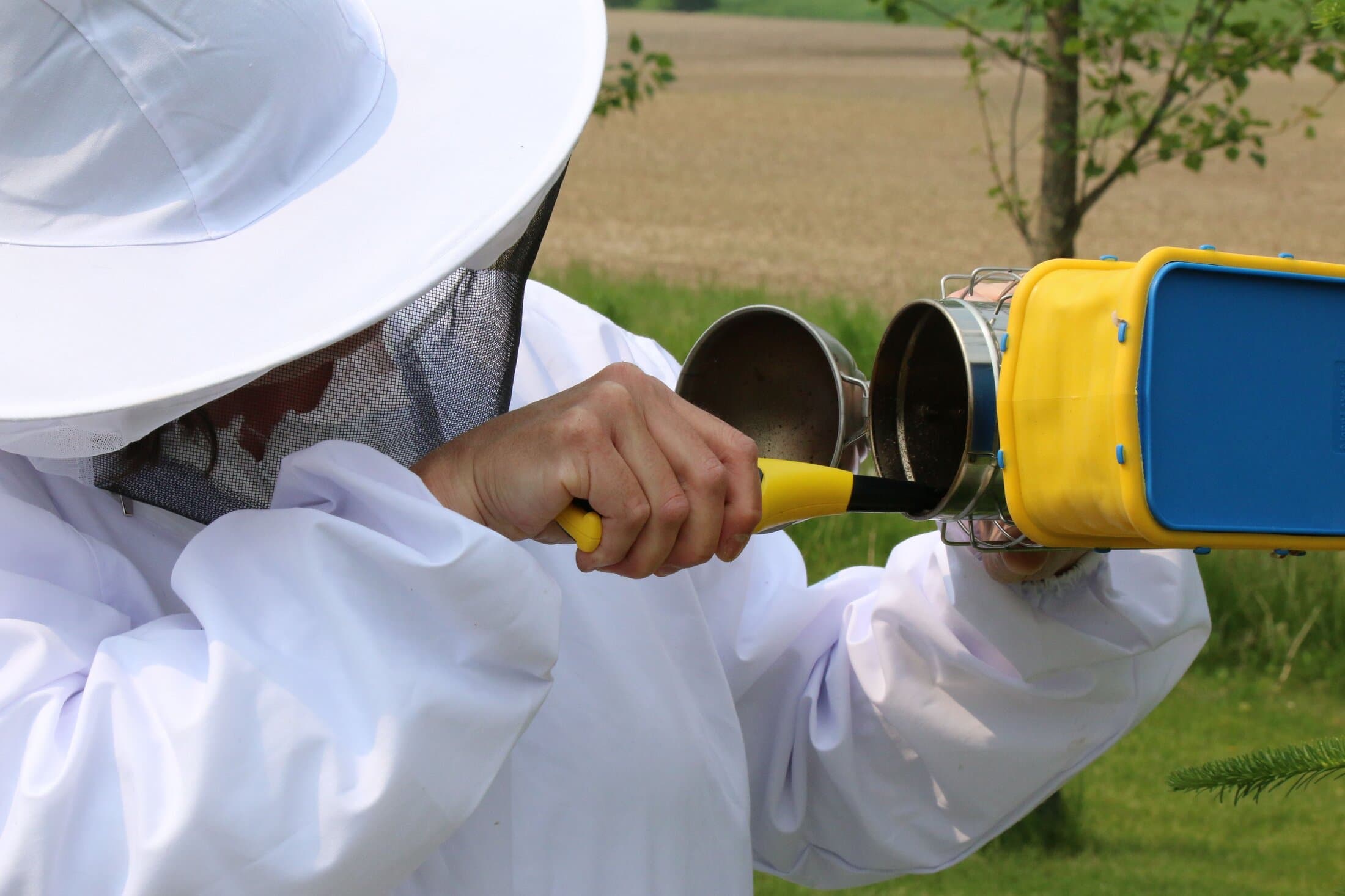 A beekeeper in a full protective suit operating a smoker